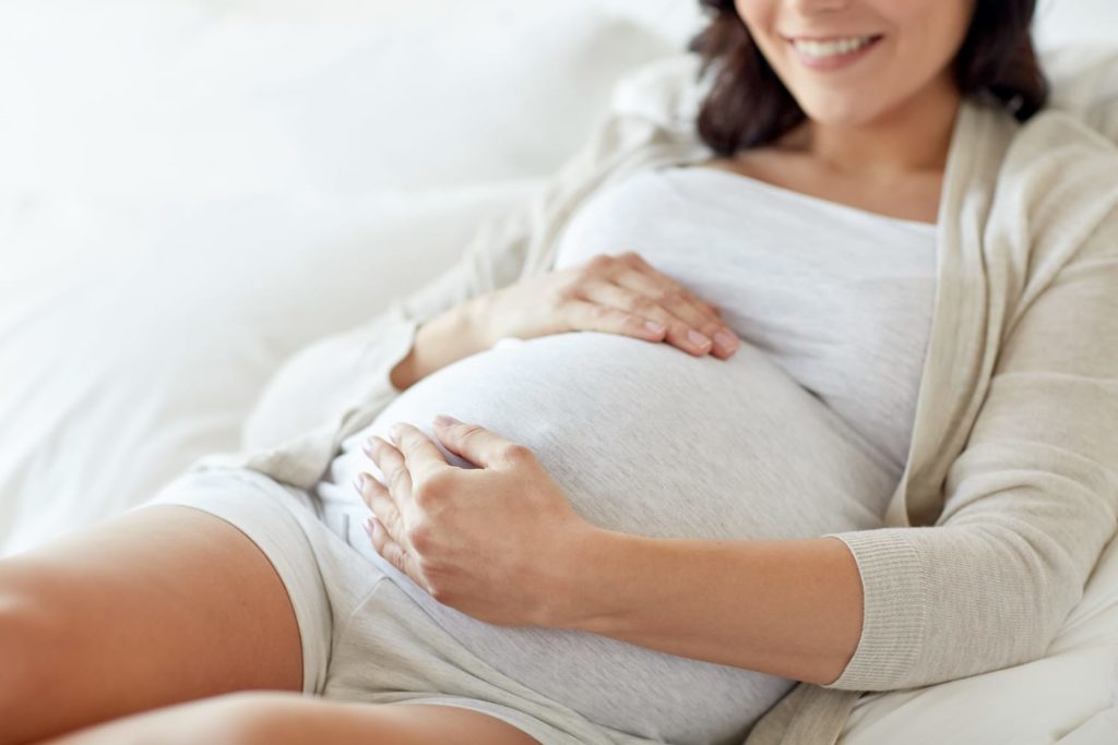 Pregnancy & Sleep: Common Issues & Tips for Sleeping Pregnant woman holding her belly in bed